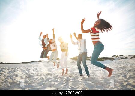Portrait verspielte, energische junge Freunde springen vor Freude am sonnigen Sommerstrand Stockfoto