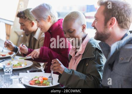 Lächelnde junge Frau, die mit Freunden Mittagessen isst Stockfoto