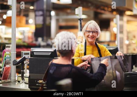 Freundliche leitende Kassiererin hilft Kunden beim bezahlen im Supermarkt Stockfoto