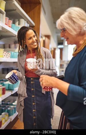 Lächelnder Arbeiter hilft Seniorinnen beim Einkaufen nach Tassen Stockfoto