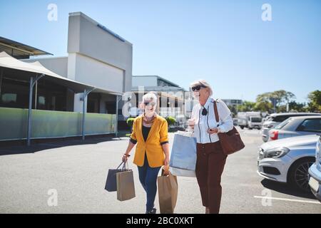 Fröhliche Seniorinnen mit Einkaufstaschen auf sonnigen Parkplätzen Stockfoto