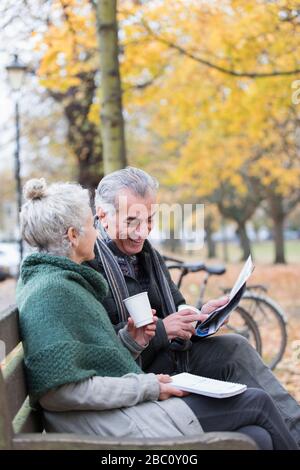 Älteres Paar liest Zeitung und trinkt Kaffee auf der Bank im Herbstpark Stockfoto