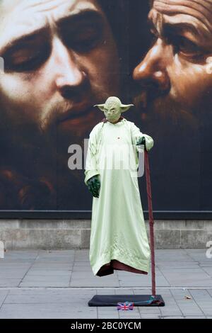 Ein Streetdarsteller, der als Star Wars-Charaktere yoda verkleidet ist, vor einer Plakatwand in der Nationalgalerie, die die Ausstellung "Beyond Caravaggi" wirbt Stockfoto