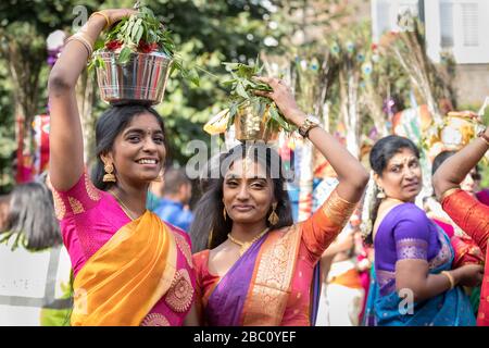 Junge Hindu-Frauen in Sari, lächelnd, während sie an einem Festzug des Chariot-Festivals teilnehmen und auf ihrem Kopf anbieten Stockfoto