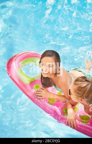 Portrait lächelnde Frauen Freunde schwimmend auf Poolfloß im Sommer-Swimmingpool Stockfoto