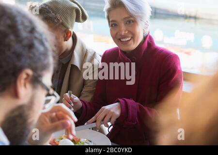 Portrait lächelnde junge Frau, die mit Freunden im Restaurant isst Stockfoto
