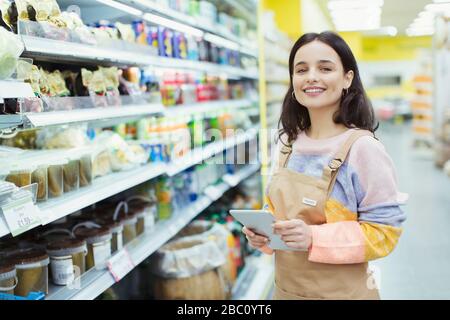 Portrait selbstbewusster, lächelnder weiblicher Lebensmittelhändler mit digitalem Tablet im Supermarkt Stockfoto