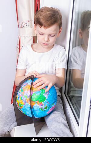 Selbstisolierungs- und Quarantänekonzept. Ein siebenjähriger Quarantänejunge studiert den Globus und träumt von Reisen Stockfoto