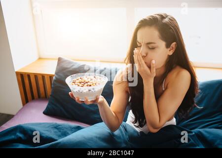 Junge schöne Frau im Morgenbett zu Hause. Weibliche Person fühlt sich krank, nachdem sie Frühstück Müsli und Cornflakes mit Milch gegessen hat. Spüren Sie Erbrechen. Ekel. Stockfoto