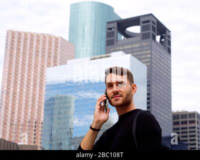 Junger selbstbewusster Geschäftsmann, der sein Telefon in der Innenstadt von Houston mit einem schönen Blick auf die Stadt verwendet. Stockfoto