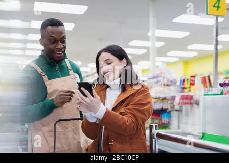 Lebensmittelhändler helfen Kunden mit Smartphone im Supermarkt Stockfoto