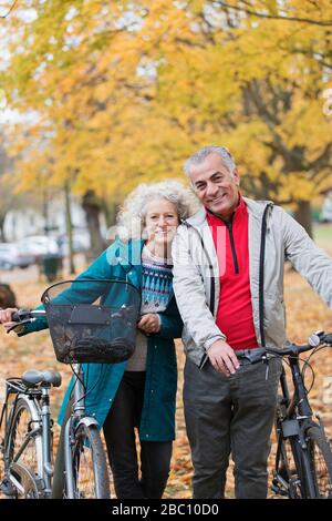 Portrait lächelndes, unbeschwertes Senioren-Paar mit Fahrrädern im Herbstpark Stockfoto