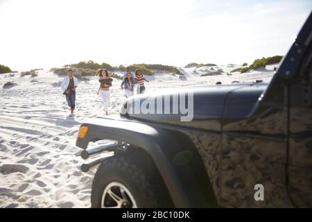 Junge Freunde, die am sonnigen Strand in Richtung Jeep laufen Stockfoto
