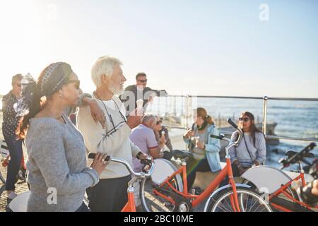 Aktive Touristen älterer Freunde mit Fahrrädern, die Eis am sonnigen Ozean essen, blicken auf Stockfoto