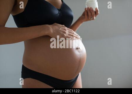 Schließen Sie die schwangere Frau, die eine Feuchtigkeitscreme auf den Magen anwendet Stockfoto