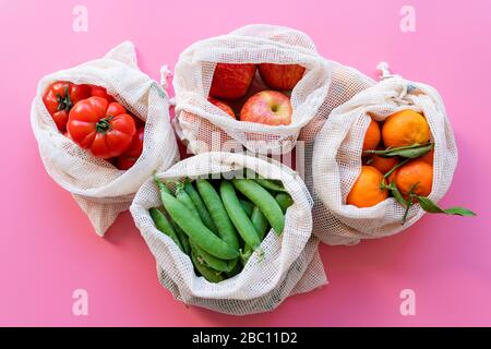 Umweltfreundliche wiederverwendbare Netzbeutel mit frischen grünen Erbsen, Tomaten, Äpfeln und Clementinen Stockfoto