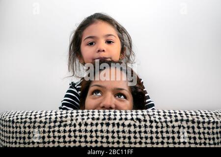 Porträt des kleinen Mädchens und ihrer Mutter versteckt hinter Rückenlehne des Liegestuhls Stockfoto