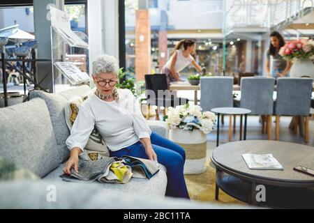 Seniorin, die Stoffschwatzen auf dem Sofa im hauseigenen Dekorgeschäft betrachtet Stockfoto