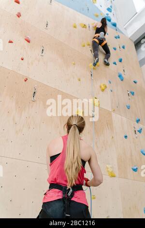 Frau mit Seilsicherungspartnerin an der Wand in der Kletterhalle Stockfoto