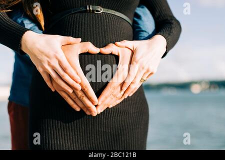 Liebevolle werdende Eltern, die mit ihren Händen am Babybauch ein Herz Formen Stockfoto