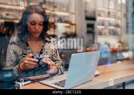 Junge Frau mit Kamera und Laptop in einem Café hinter der Fensterscheibe Stockfoto