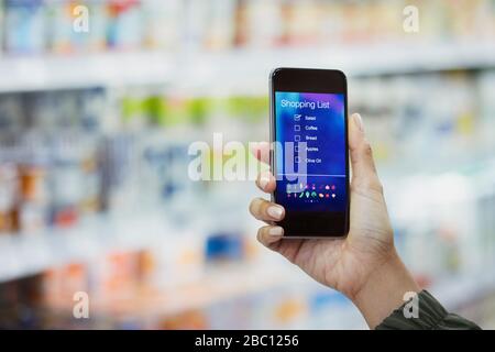 Persönliche Perspektive Frau überprüft digitale Einkaufsliste auf Smartphone im Supermarkt Stockfoto