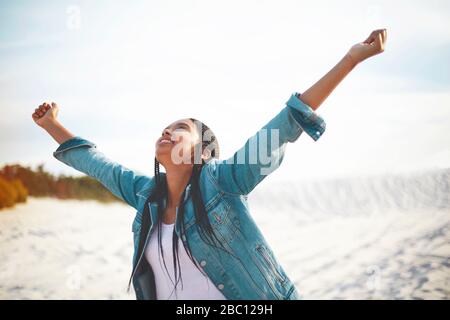 Überschwängliche junge Frau mit am Strand ausgestreckten Armen Stockfoto