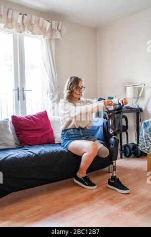 Junge Frau mit Beinprothese sitzt zu Hause auf der Couch Stockfoto