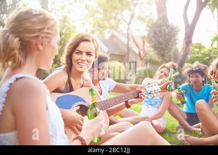 Junge Frauenfreunde hängen aus, spielen Gitarre und trinken Bier im Sommergras Stockfoto