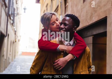 Glücklicher junger Mann, der Freundin Huckepack in einer Gasse in der Stadt Florenz, Italien trägt Stockfoto