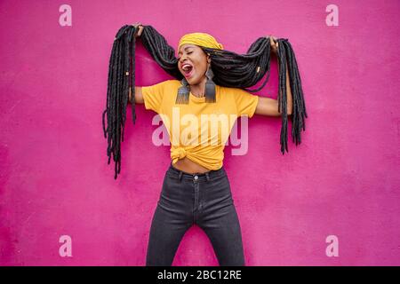 Porträt einer Frau mit langen Dreadlocks, die ihr Haar vor einer rosa Wand hält Stockfoto