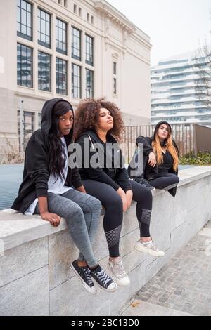 Drei sportliche junge Frauen sitzen an einer Wand in der Stadt Stockfoto