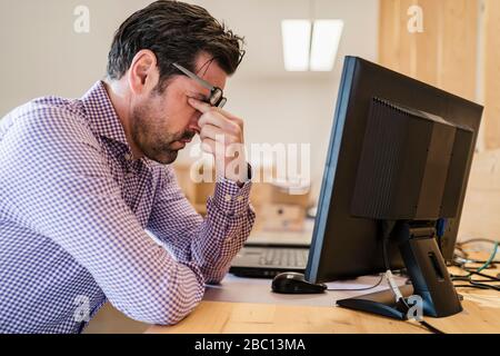 Müde Geschäftsmann am Schreibtisch in Holz-Büro mit offenem Schnitt Stockfoto