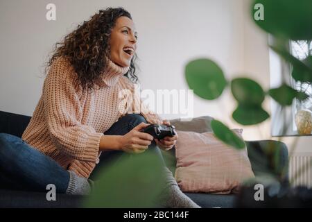 Frau sitzt auf der Couch, Spaß haben, mit einer Spielkonsole spielen Stockfoto