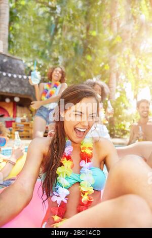 Begeisterte, lachende junge Frau, die im Sommer-Schwimmbad Lei trägt Stockfoto