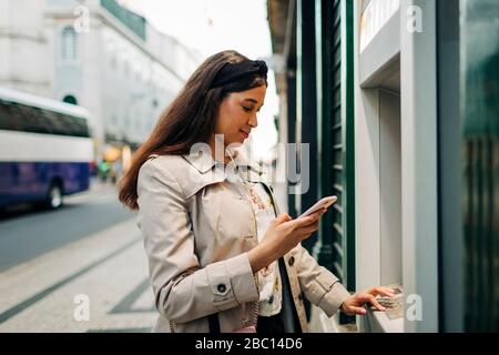 Frau mit geldautomat und Handy Stockfoto