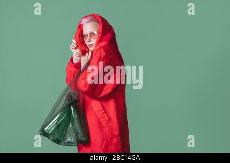 Porträt der jungen Frau mit kurzen rosa Haaren trägt roten Mantel halten Beutel mit Plastikflaschen Stockfoto