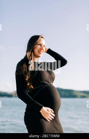 Glückliche schwangere junge Frau am Wasser Stockfoto