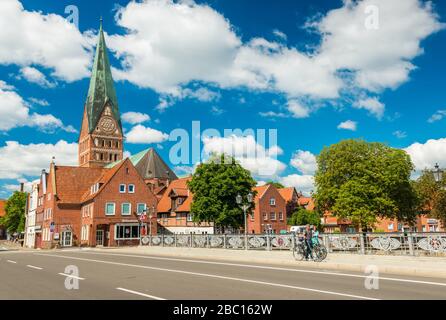 Lüneburg - Juli 2018, Niedersachsen, Deutschland: Menschen zu Fuß über die Brücke. Dom und Alte historische Häuser mit blauem Himmel und Wolken auf der Rückseite Stockfoto