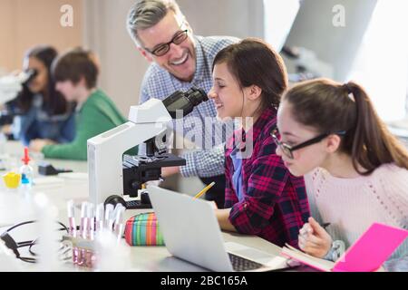 Lächelnde wissenschaftliche Lehrerin, die Mädchen bei wissenschaftlichen Experimenten am Mikroskop im Labor hilft Stockfoto