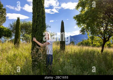 Frau auf der Wiese, umarmt Zypresse Stockfoto