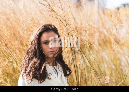 Junge Frau posiert für ein Fotoporträt vor einem Busch aus dickem Gras, sehr nettes millenials Mädchen posiert Stockfoto