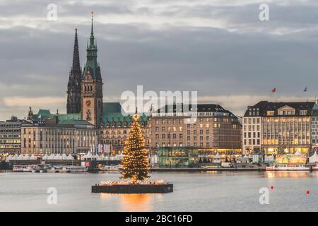 Deutschland, Hamburg, beleuchteter Alstertanne Baum in der Dämmerung mit Jungfernstieg Promenade und St. Nikolaus Kirche im Hintergrund Stockfoto