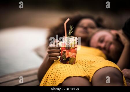 Junge Frau liegt auf dem Boden mit ihrem Freund hält frischen Eistee trinken Stockfoto