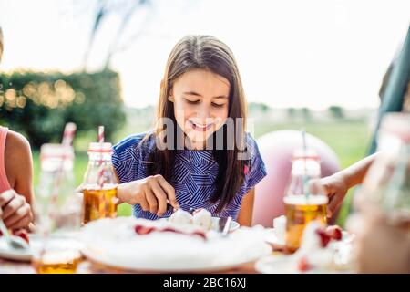 Happy girl essen Stück Kuchen auf einer Geburtstagsfeier im Freien Stockfoto
