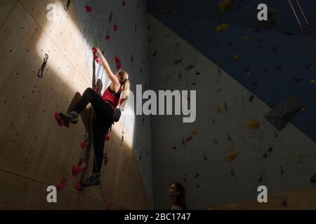 Frau klettert an der Wand in der Kletterhalle mit Sonnenlicht und Schatten Stockfoto