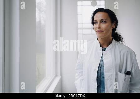 Ärztin schaut aus dem Fenster und lächelt Stockfoto