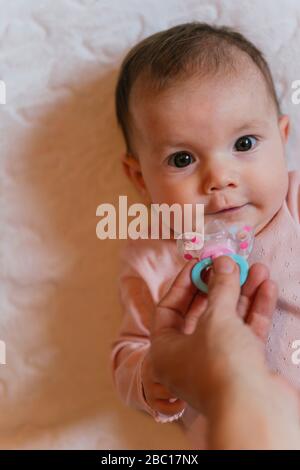 Mutter Hand gibt den Schnuller Baby Mädchen auf dem Bett liegen Stockfoto