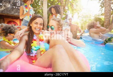Portrait begeisterte, lachende junge Frauen Freunde trinken und spielen im Sommer-Schwimmbad Stockfoto