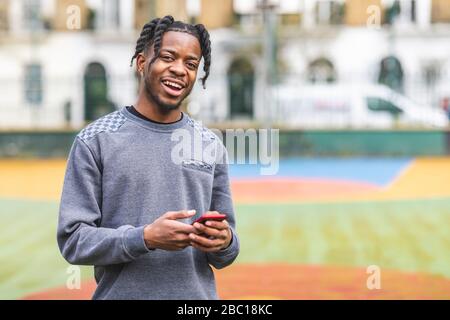 Lachender junger Mann, der Smartphone hält, die Kamera anschaut Stockfoto
